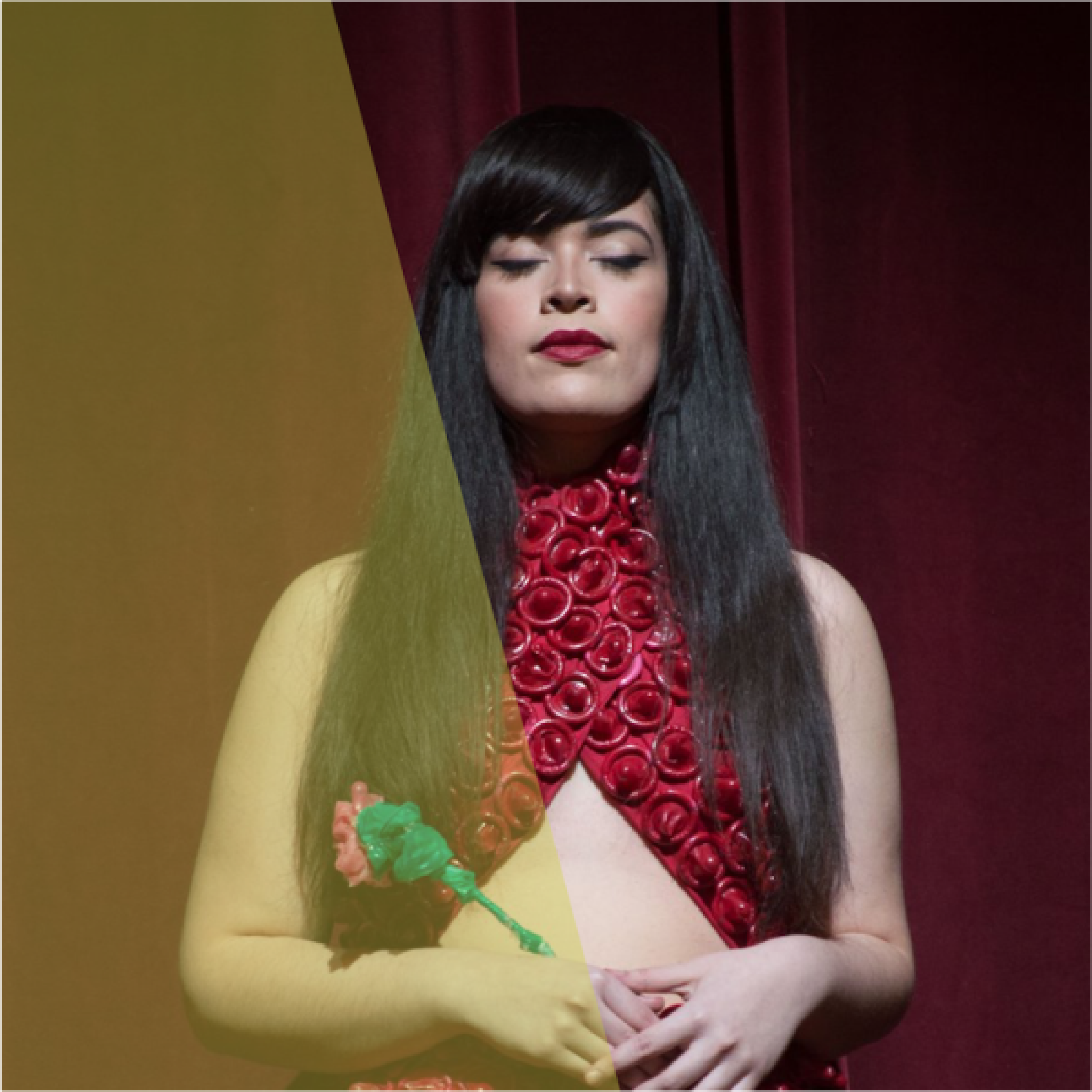 Woman wearing a condom dress with a red velvet curtain behind her.